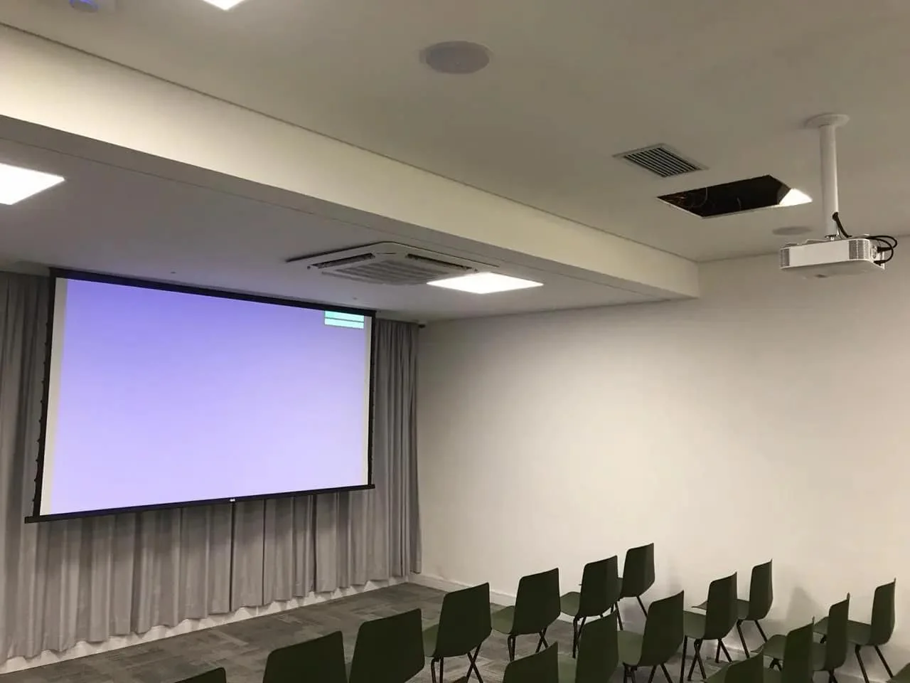 Auditório com tela de projeção e cadeiras em fileiras.