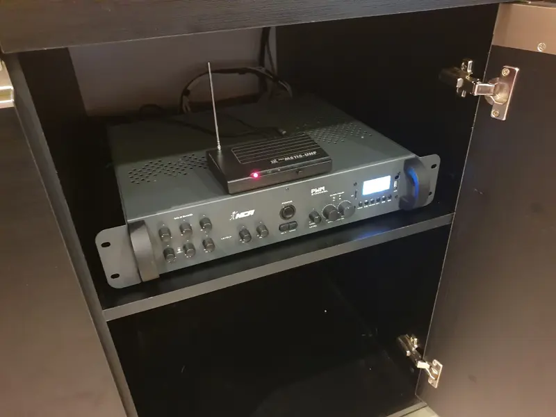 Amplificador de som ambiente instalado dentro de armário, com receptor de microfone sem fio.