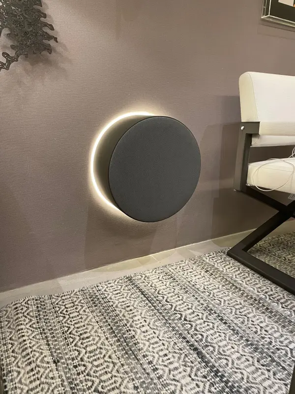 Caixa acústica redonda com luz de contorno, na parede de um ambiente interno da Mostra Magna Audio.