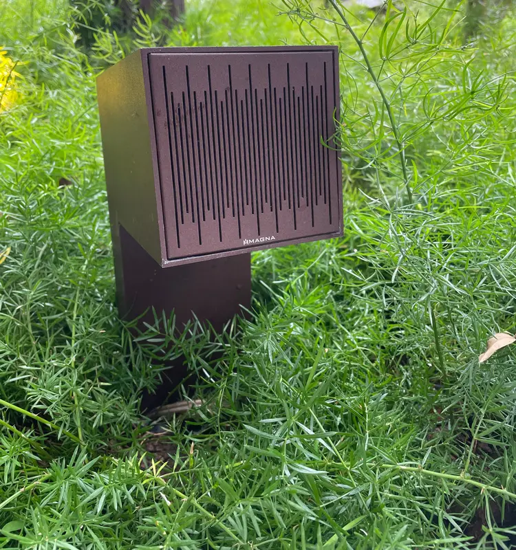 Caixa acústica de jardim Magna Audio no meio da vegetação, na área externa da mostra.
