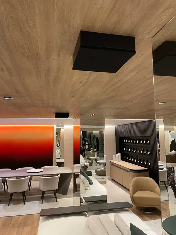 Estar e jantar da Mostra Magna Audio, com forro de madeira, caixas de sobrepor no teto e parede iluminada em degradê.