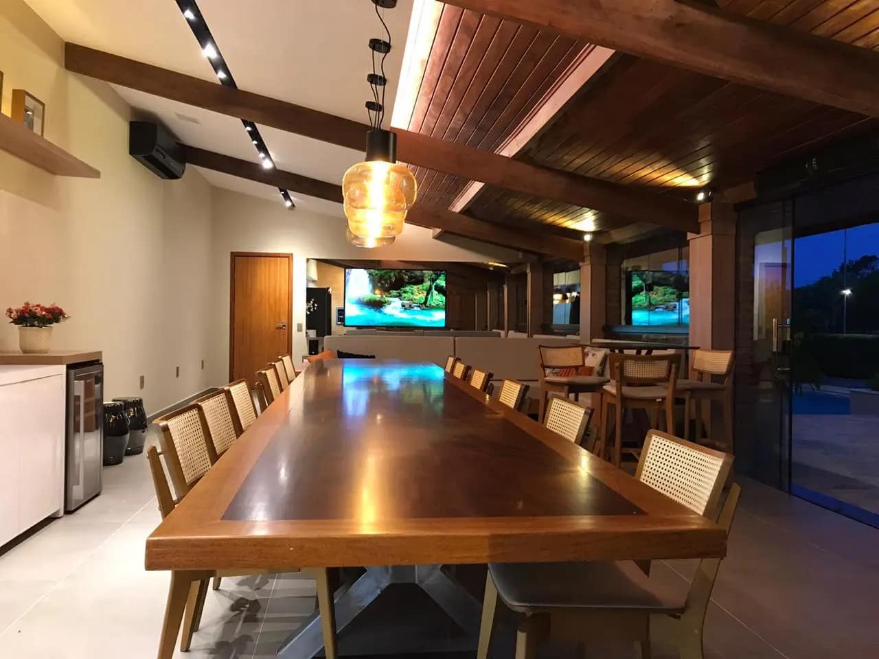 Espaço gourmet com mesa longa, iluminação em cena e monitor ao fundo.