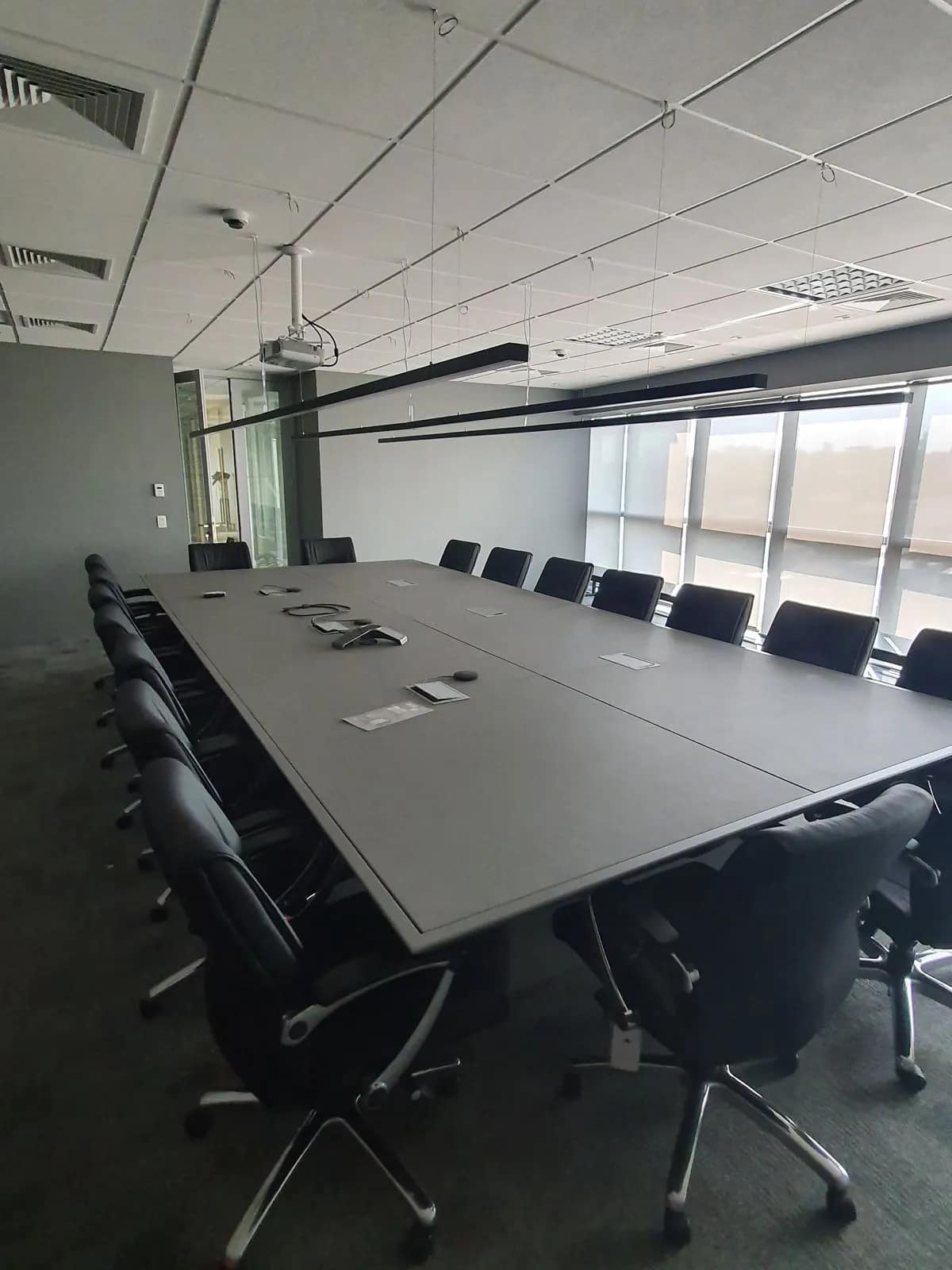 Sala de reunião de mesa longa, com tela e câmera alinhadas ao eixo da mesa.