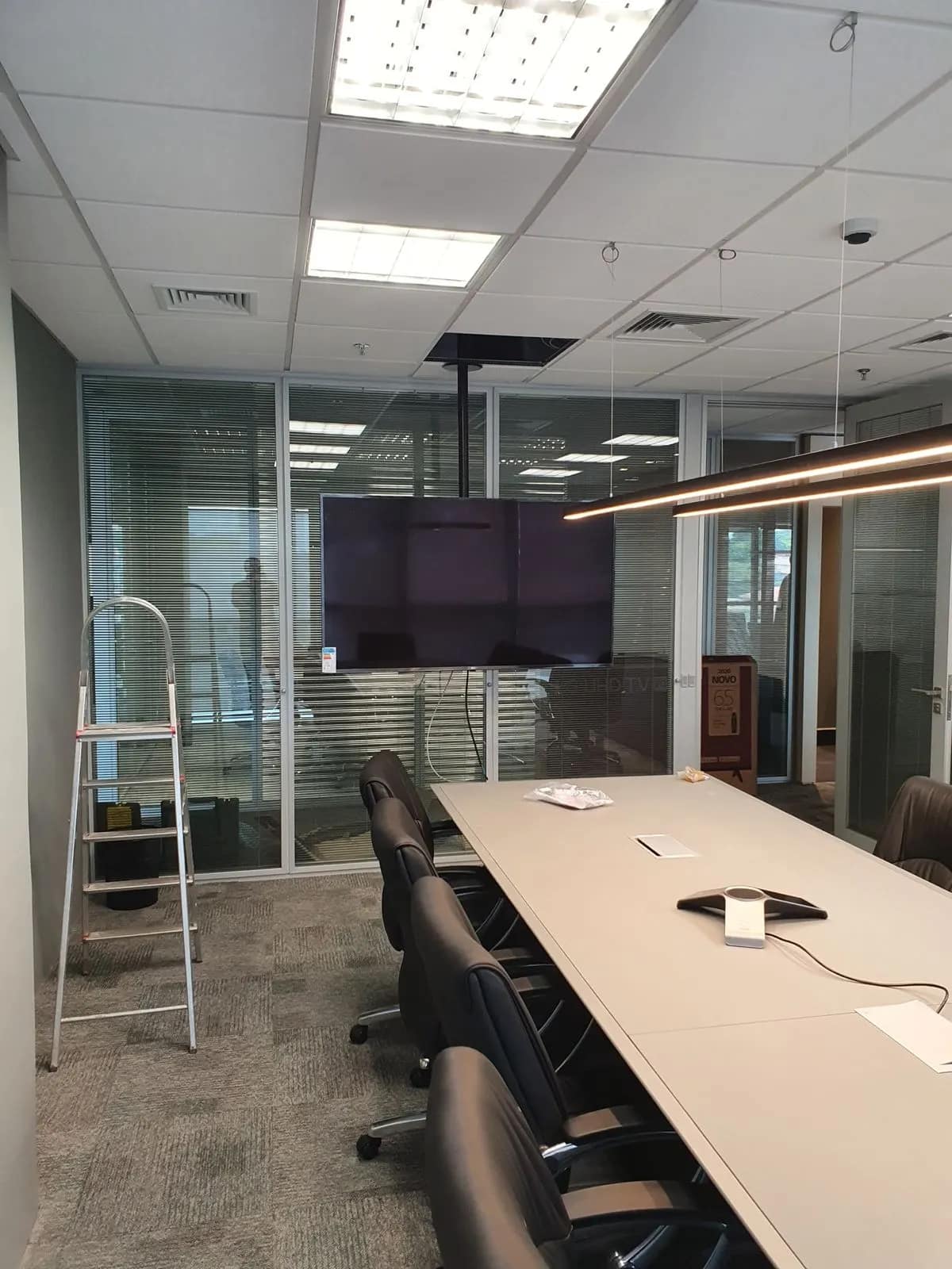 Sala de reunião envidraçada, com monitor em coluna e ponto de energia na mesa.