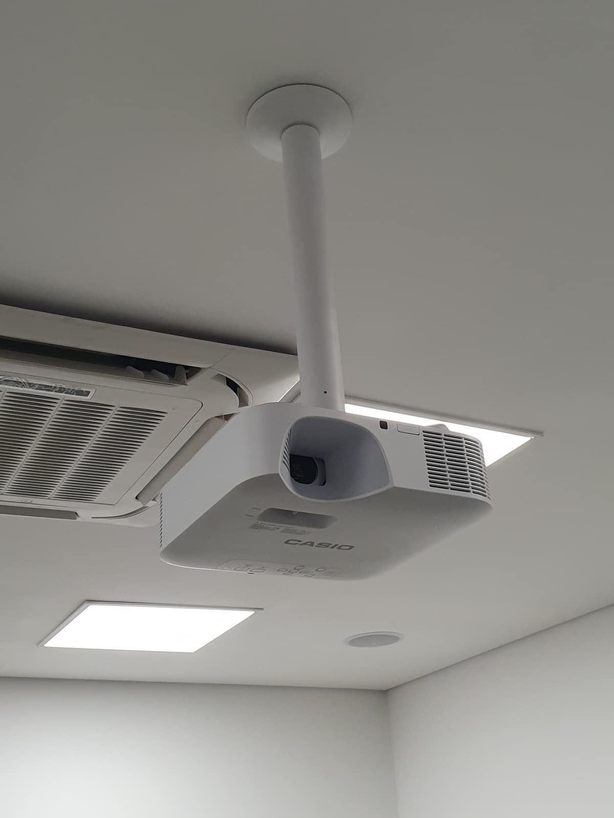 Projetor fixado no teto por tubo, com a luz e o ar-condicionado no mesmo forro.
