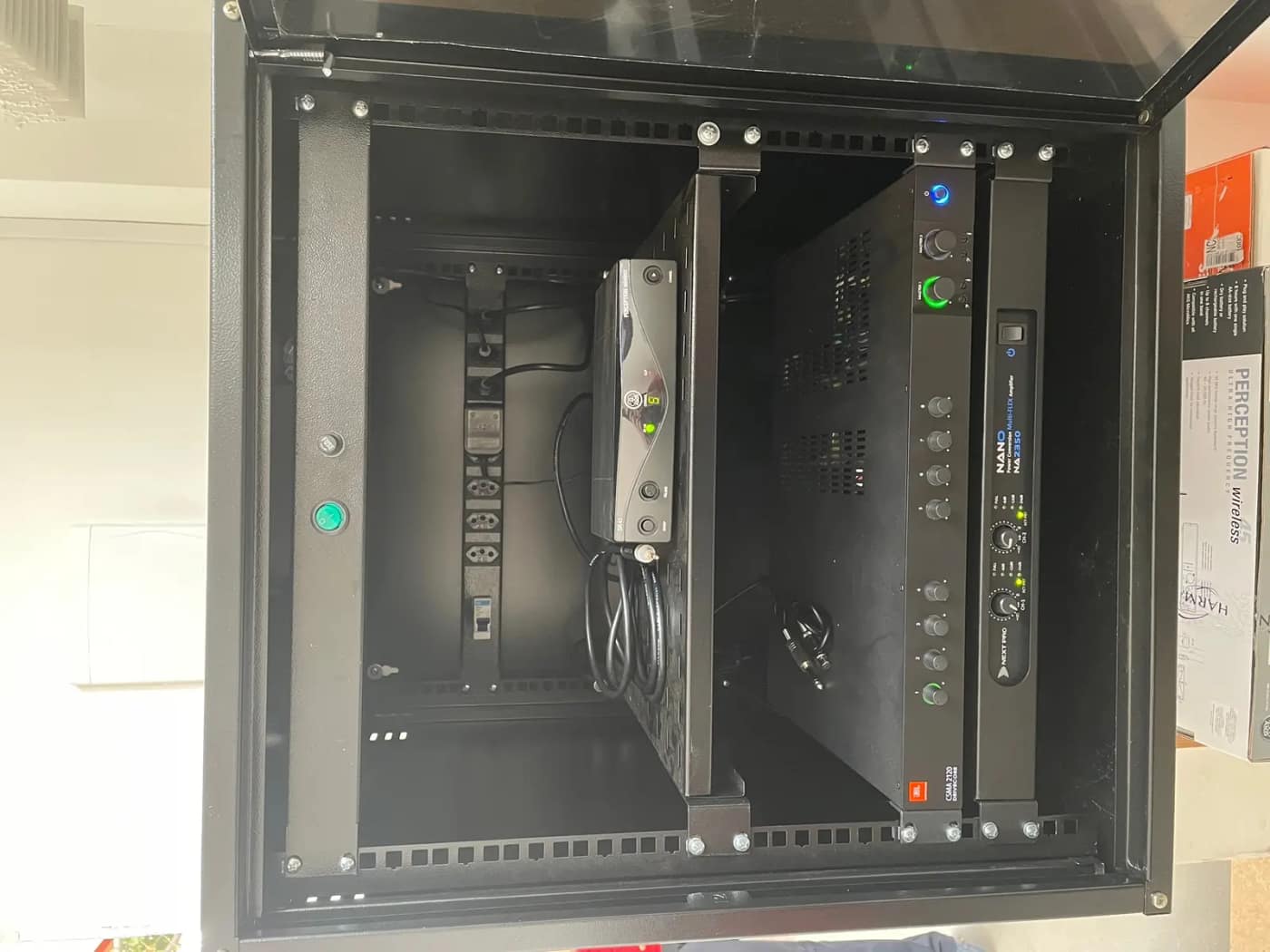 Rack de equipamentos aberto, com amplificadores, receptor de microfone sem fio e régua de energia organizados.