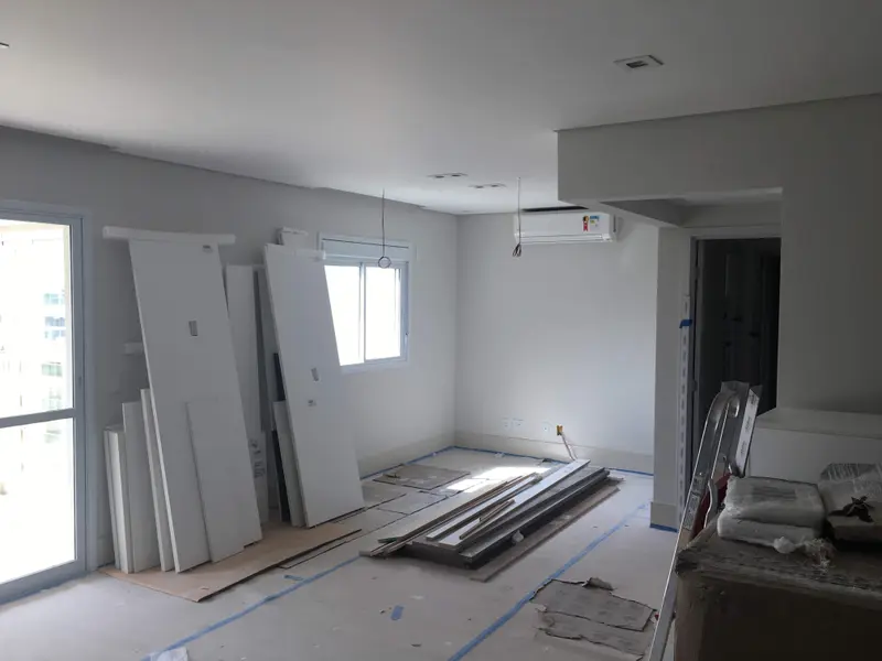 Sala de apartamento em obra, com placas de forro e materiais no piso, antes da instalação.