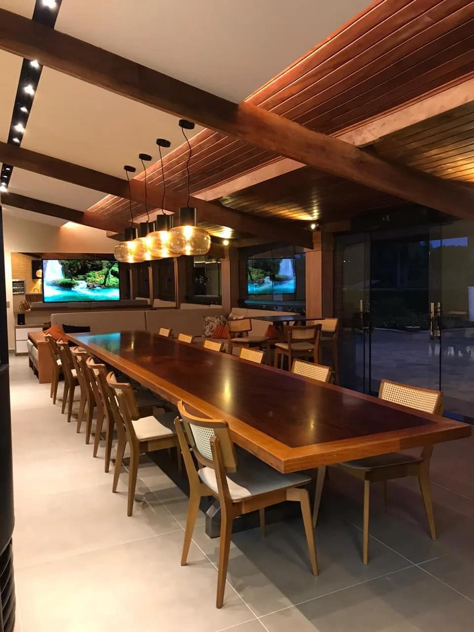 Área gourmet com mesa longa, pendentes e monitor integrado à marcenaria.