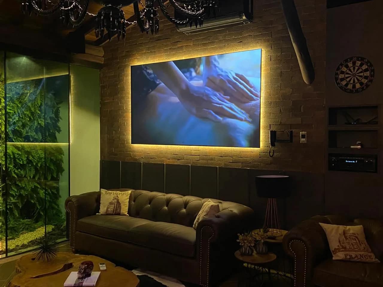 Sala com sofá de couro, jardim vertical e tela de projeção grande iluminada por trás.
