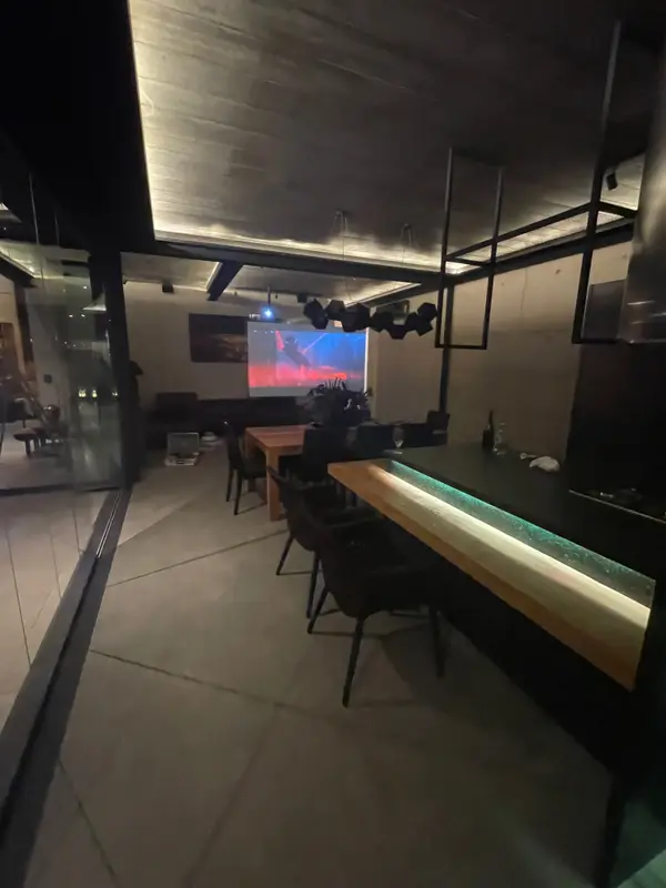 Balcão do espaço gourmet com luz embutida no tampo, mesa de jantar e projeção ao fundo.