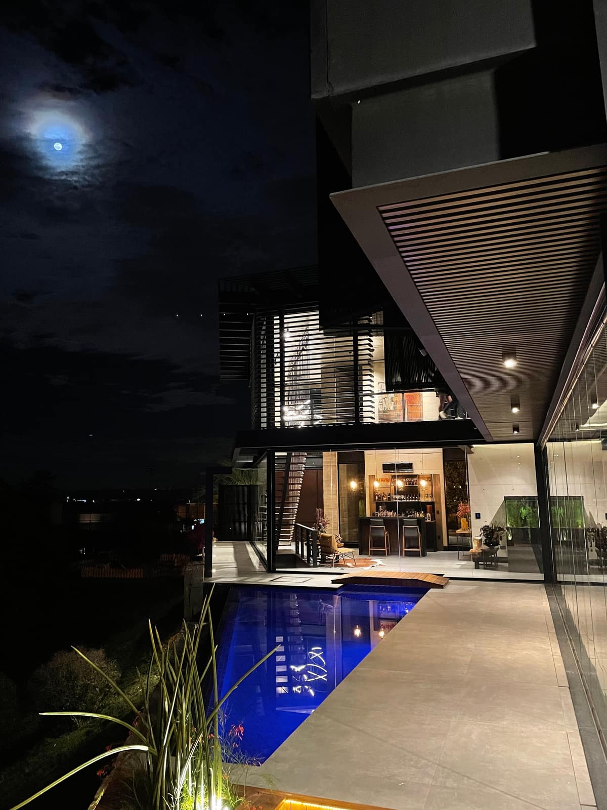 Casa à noite vista da piscina, com a área social acesa e a luz do jardim.