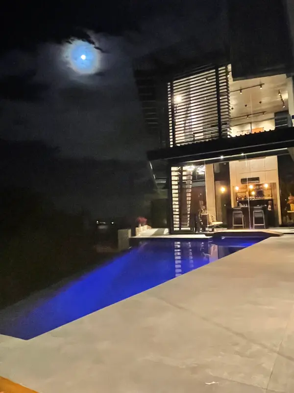 Piscina com luz azul à noite e a área social da casa acesa.