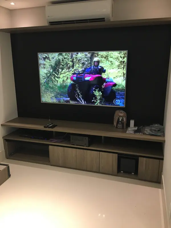 Sala de TV de apartamento com sistema 5.1, TV na parede escura e rack de marcenaria.