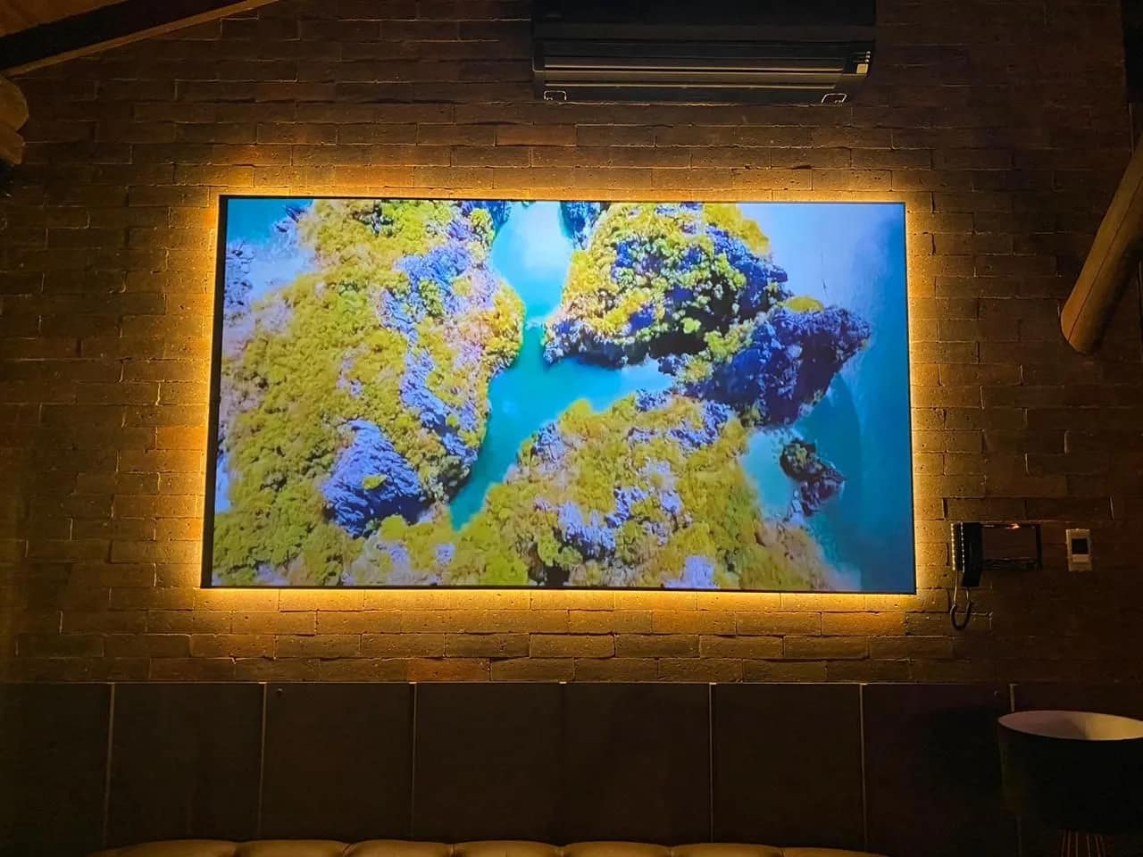Monitor grande embutido em parede de tijolo, com iluminação por trás.