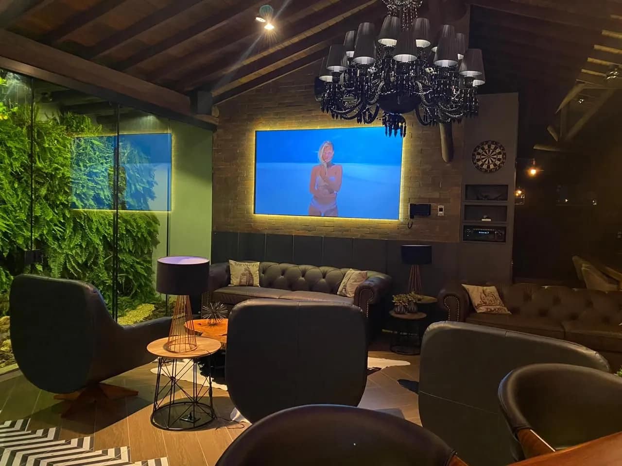 Sala com tela de projeção, jardim vertical e iluminação cênica.