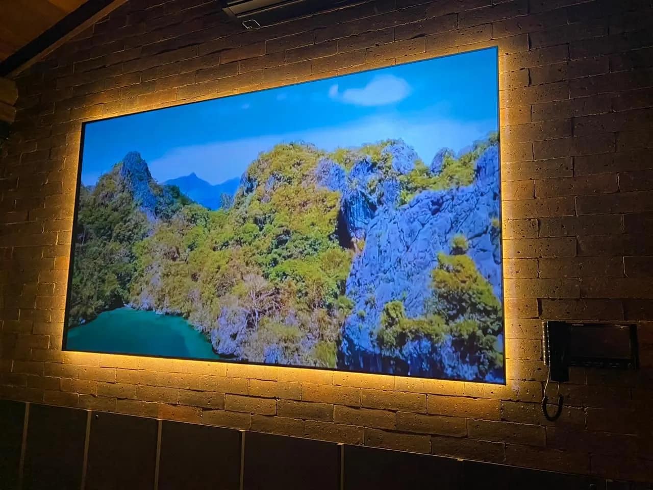 Tela de projeção iluminada por trás em parede de tijolo.