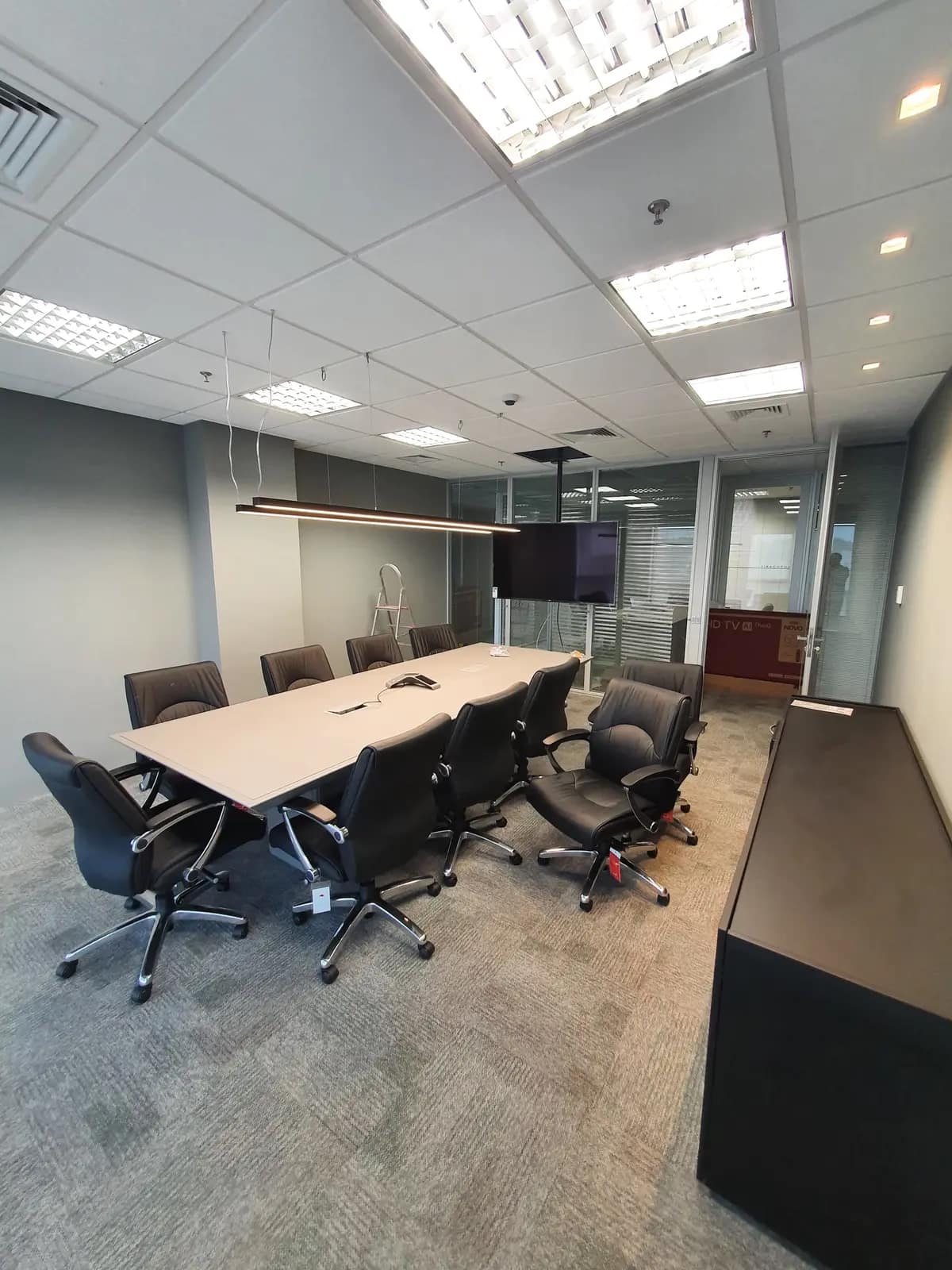 Sala de reunião corporativa com mesa de reunião, cadeiras e monitor ao fundo.