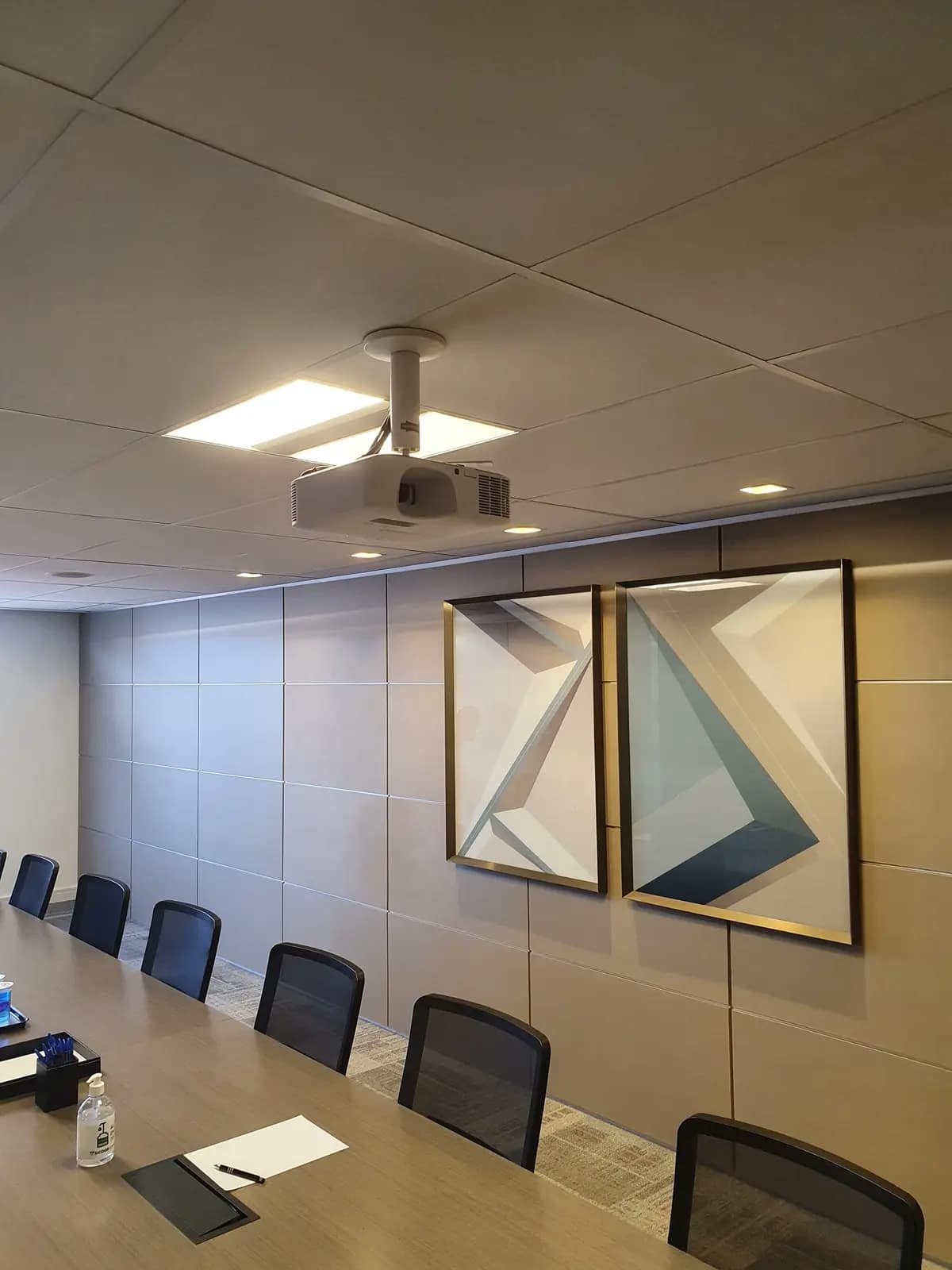 Sala de treinamento com projetor fixado no teto e painéis decorativos na parede.