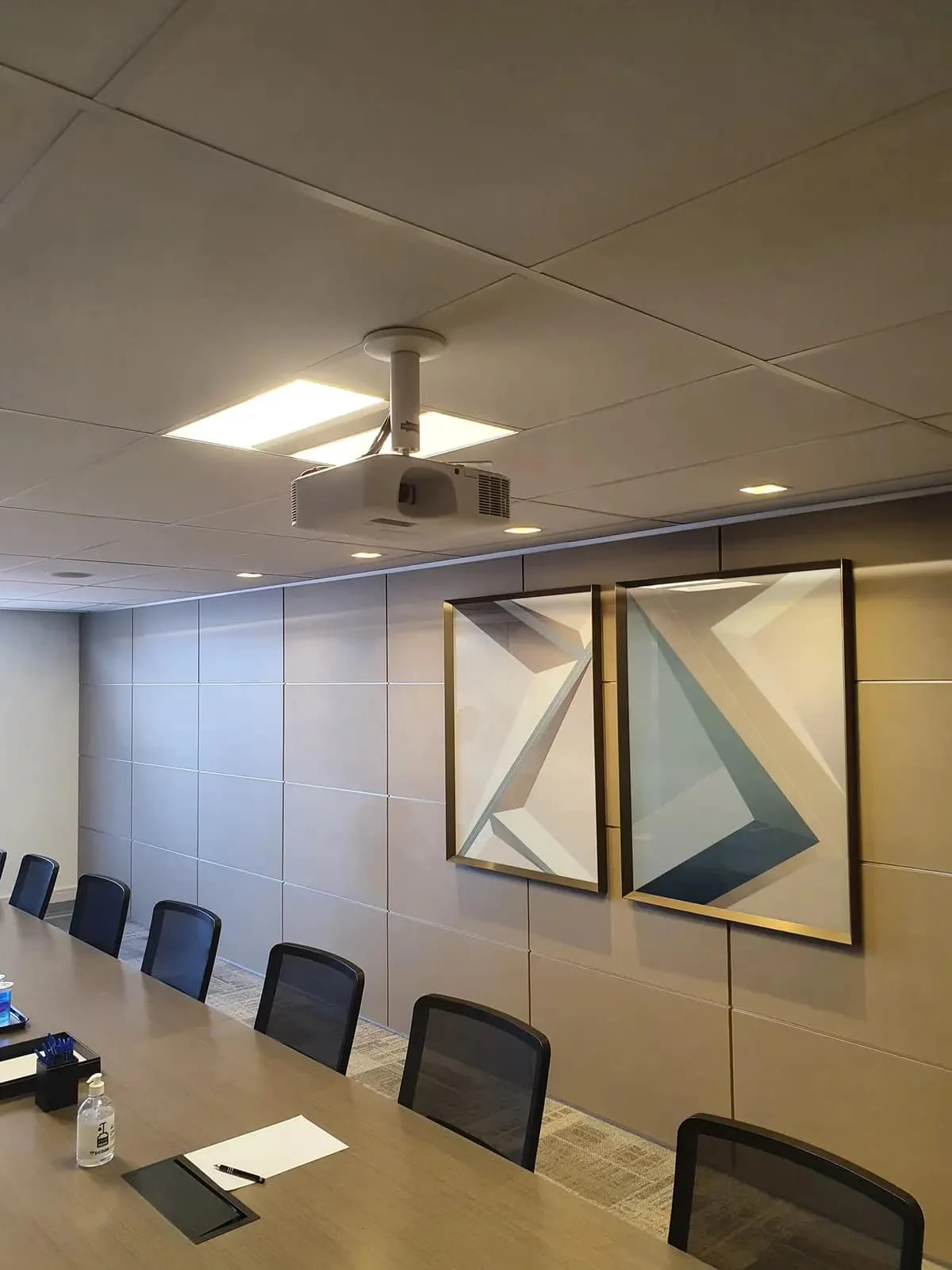 Sala de treinamento com projetor fixado no teto e painéis decorativos na parede.