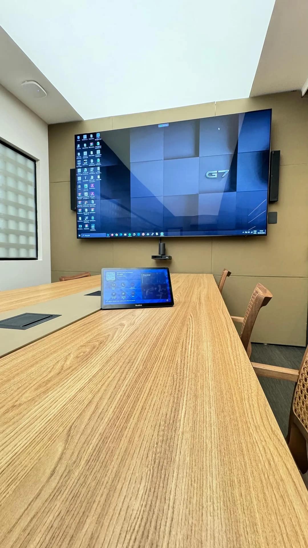 Sala com monitor grande e painel Yealink na mesa.