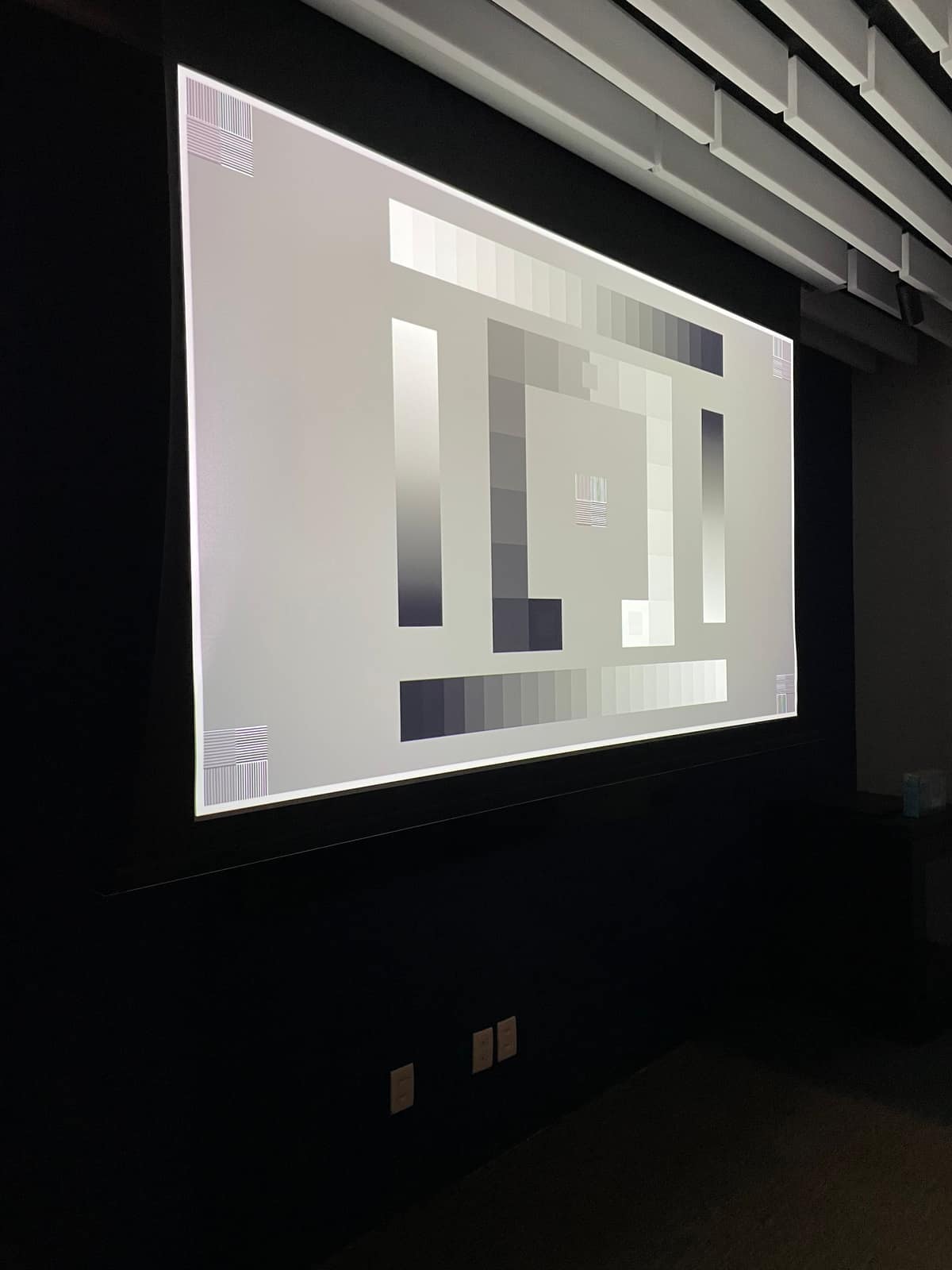 Sala escura com painéis acústicos e tela de projeção durante a calibração da imagem.