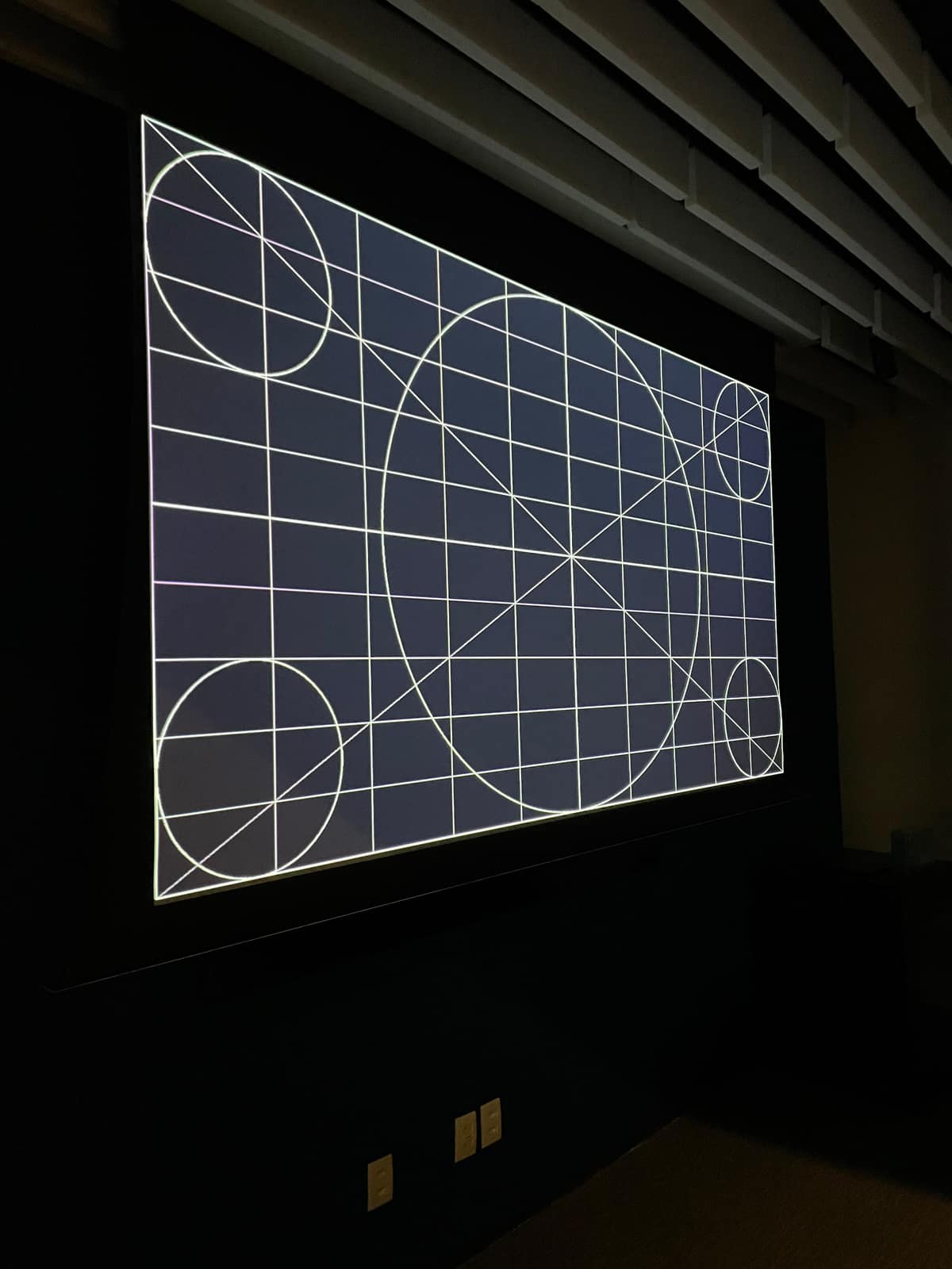 Sala com painéis acústicos e tela de projeção exibindo o padrão de ajuste da imagem.