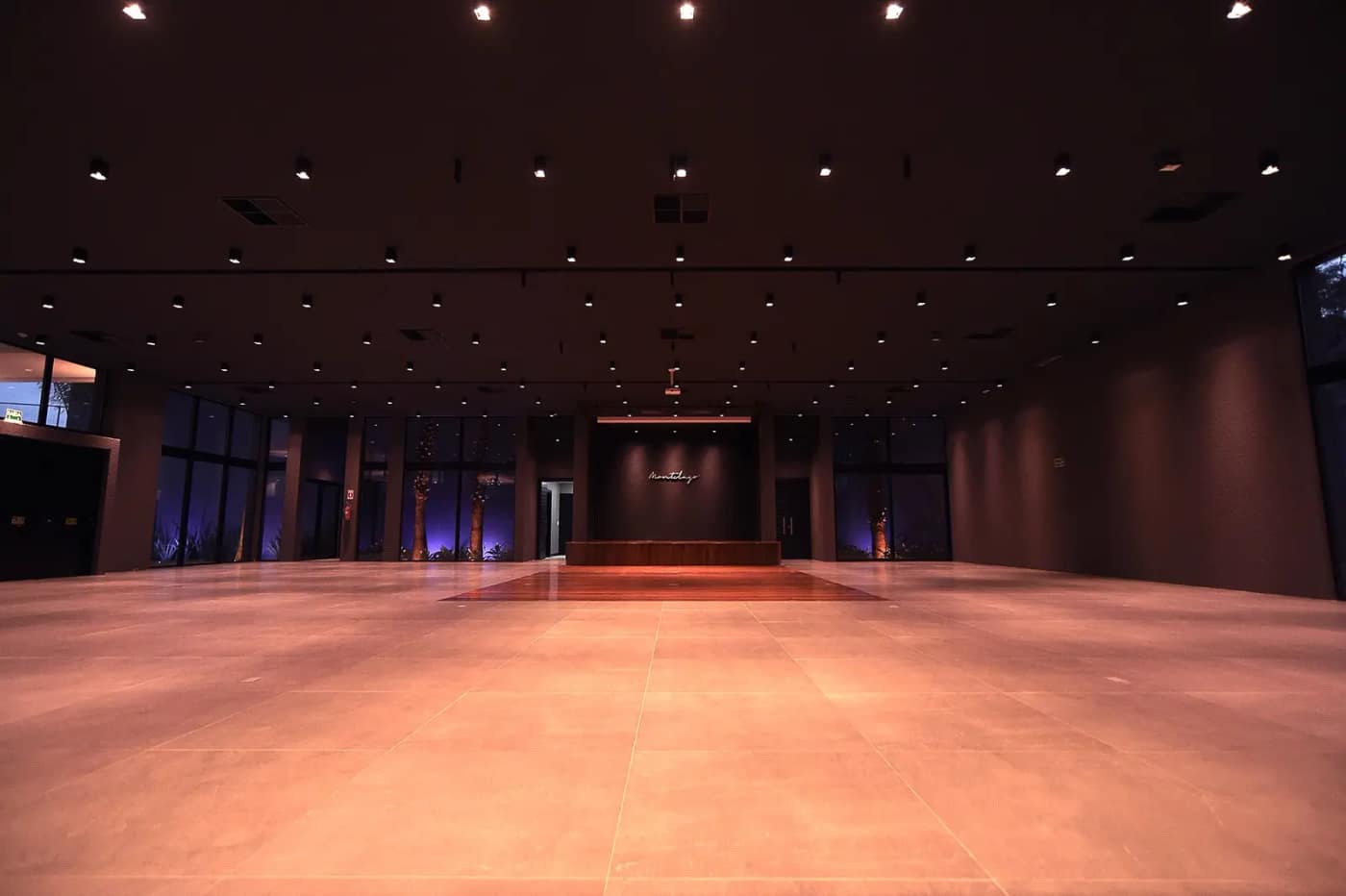 Salão de eventos preparado, com iluminação cênica e piso livre para montagem.