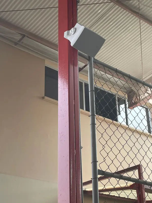 Caixa de som fixada na coluna metálica da quadra coberta de uma escola.