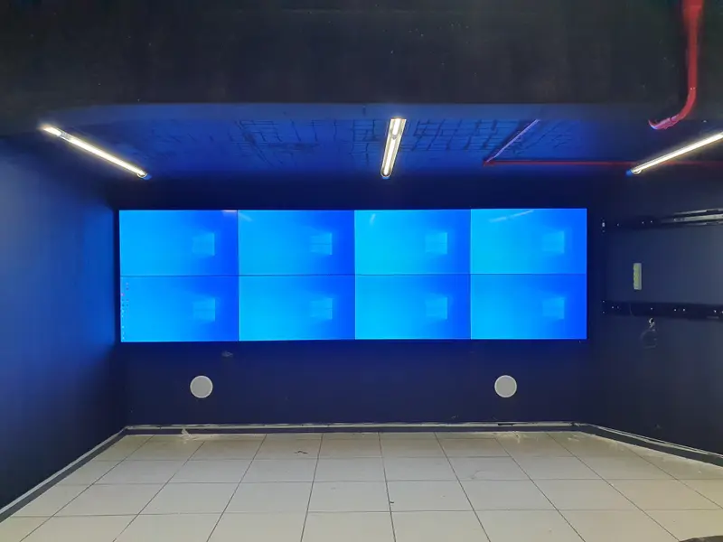 Video wall de oito telas aceso em sala de crise, com paredes escuras e sala ainda vazia.
