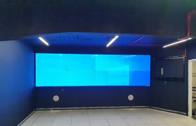Video wall exibindo uma imagem contínua em toda a parede, em sala de crise com paredes escuras.