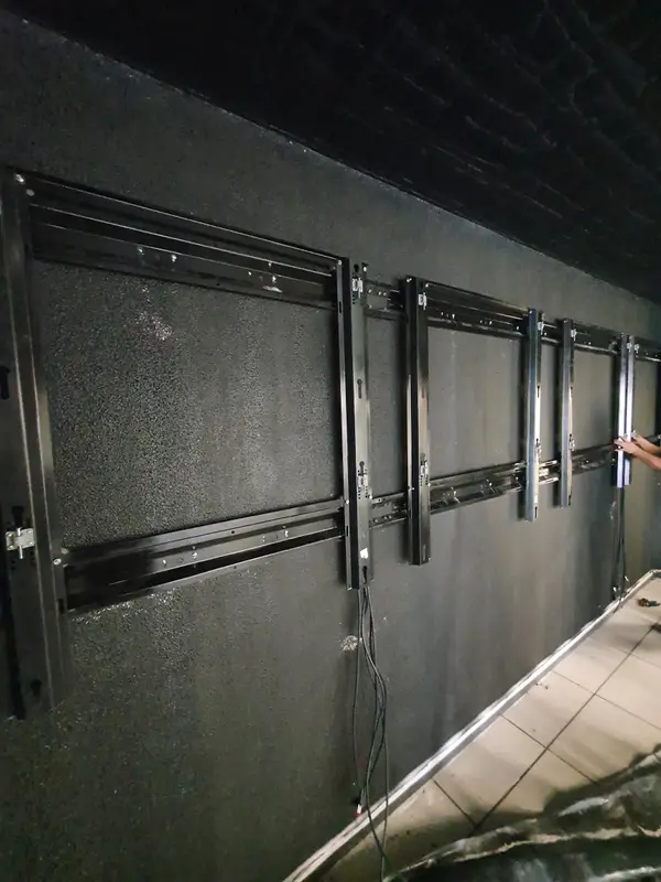 Suportes metálicos do video wall fixados na parede com revestimento acústico escuro, antes das telas.